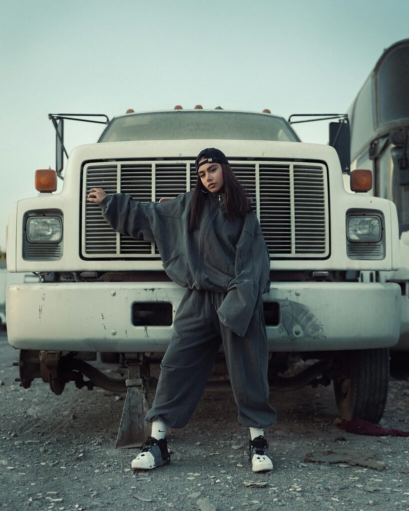 A stylish portrait of a woman in urban fashion standing in front of a large truck.